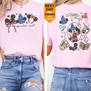 May include: A light pink t-shirt featuring Disney-themed graphics. The front displays Mickey Mouse ears, a wizard hat, and Minnie Mouse ears with text that reads "Some imagination, huh?" The back showcases Mickey Mouse as a wizard.