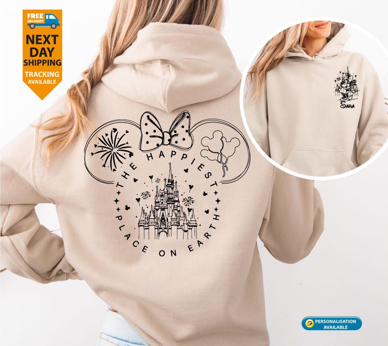 May include: Beige hoodie with a black graphic on the back featuring a castle, bow, fireworks, and balloons, with the text "THE HAPPIEST PLACE ON EARTH." A smaller graphic is on the front. The hoodie has a drawstring hood and a front pocket.