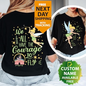 May include: Black t-shirt with a Tinkerbell design and the words "We All Have The Courage To Fly". The design includes stars, a castle, and the phrase "You can fly by you can fly!" in a whimsical font. The shirt also has a design on the right side.