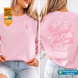 May include: A light pink sweatshirt with a bow and the text "the most magical place on earth" in pink. The sweatshirt has a small bow graphic on the front. Walt Disney World is printed below the text.