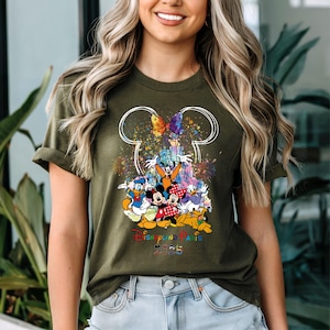 May include: A green t-shirt with a white outline of Mickey Mouse ears and a colorful graphic of Mickey Mouse and friends in front of the Disneyland Paris castle. The text "Disneyland Paris 2023" is printed below the graphic.