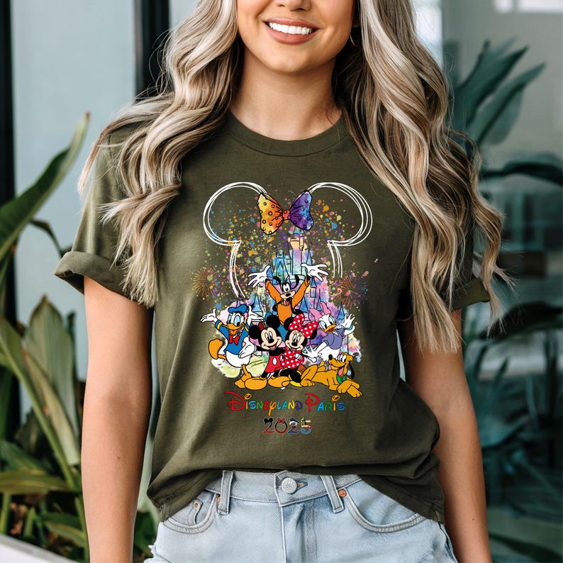 May include: A green t-shirt with a white outline of Mickey Mouse ears and a colorful graphic of Mickey Mouse and friends in front of the Disneyland Paris castle. The text "Disneyland Paris 2023" is printed below the graphic.
