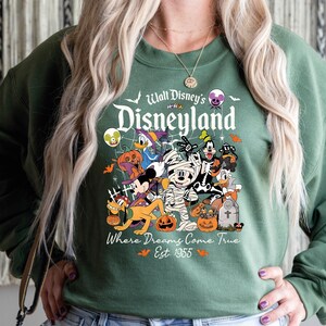 May include: Green sweatshirt with a Halloween Disneyland graphic. The design features Disney characters in costumes, pumpkins, and the text "Walt Disney's Disneyland" and "Where Dreams Come True Est. 1955".