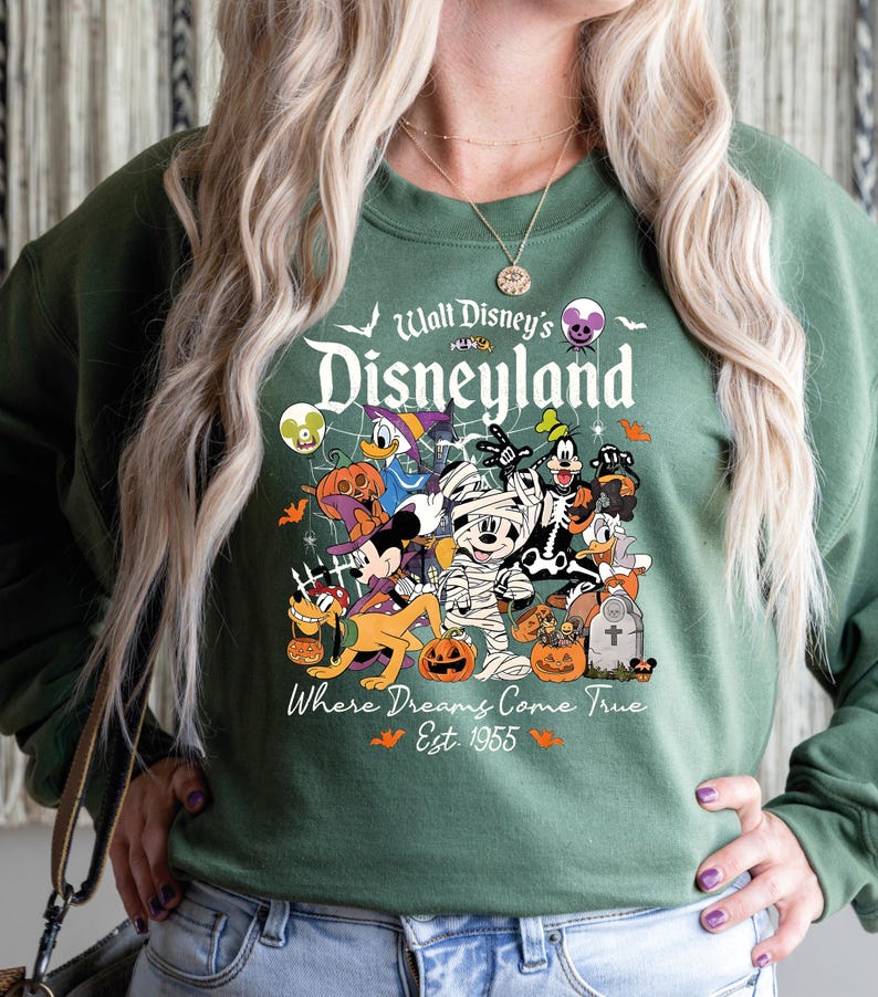 May include: Green sweatshirt with a Halloween Disneyland graphic. The design features Disney characters in costumes, pumpkins, and the text "Walt Disney's Disneyland" and "Where Dreams Come True Est. 1955".