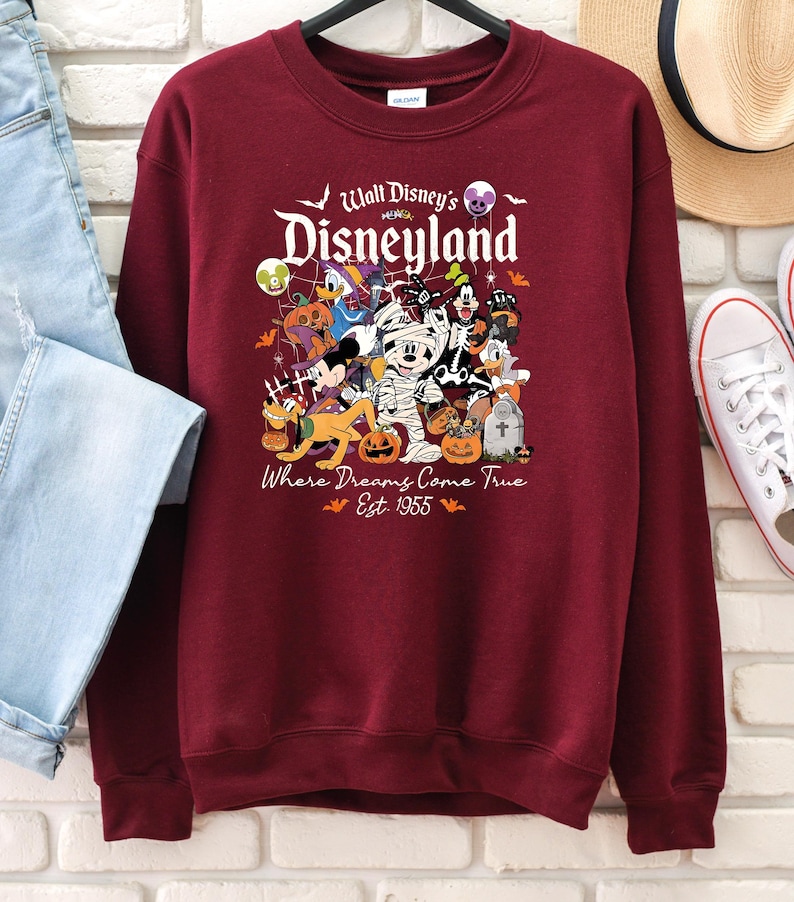 May include: Burgundy crew neck sweatshirt with a Disneyland Halloween design. The graphic features Mickey Mouse, Donald Duck, and other Disney characters in Halloween costumes. Text reads "Walt Disney's Disneyland" and "Where Dreams Come True Est. 1955".