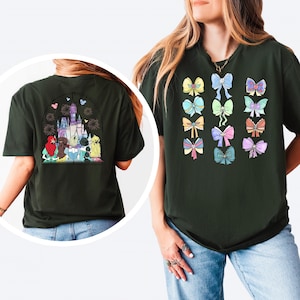 May include: A dark green t-shirt with a graphic of a castle and princesses on the back. The front of the shirt features a row of colourful bows.