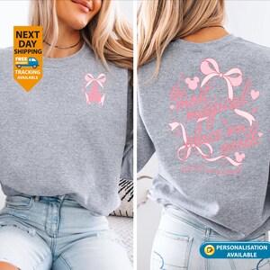 May include: A heather gray sweatshirt with a pink bow design on the front and back. The back of the sweatshirt features the text "It's a magical world on earth" in pink script with bow and Mickey Mouse head accents.