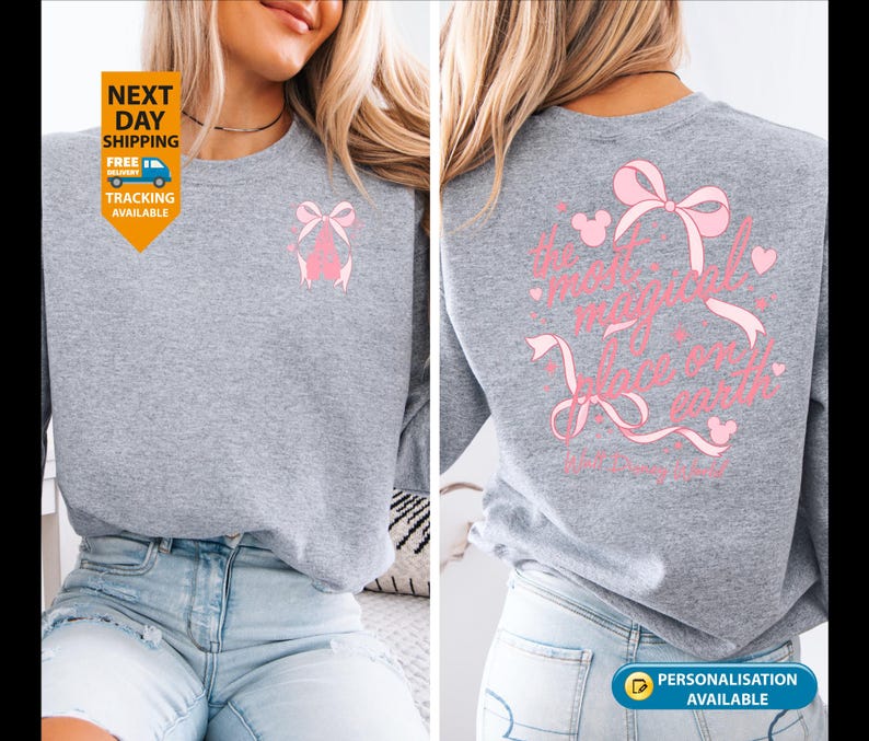 May include: A heather gray sweatshirt with a pink bow design on the front and back. The back of the sweatshirt features the text "It's a magical world on earth" in pink script with bow and Mickey Mouse head accents.