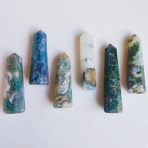 May include: Six polished agate crystal points in various shades of green, blue, and white. The points are arranged in a row on a white surface.