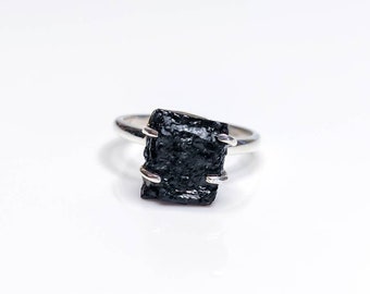 Puede incluir: Un anillo de plata con una piedra preciosa negra en bruto. El anillo es simple y elegante.