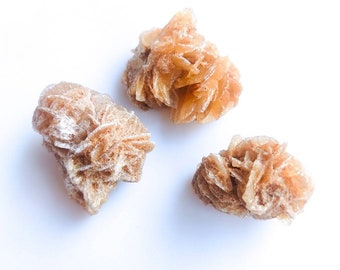 Peut inclure: Trois cristaux de quartz rose de différentes tailles et formes. Les cristaux sont de couleur brun clair et ont une surface rugueuse et texturée.