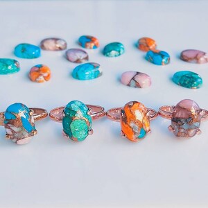 May include: Four rings with oval-shaped turquoise, copper, and pink stones set in rose gold. The stones have a mix of blue, green, orange, and pink colors.