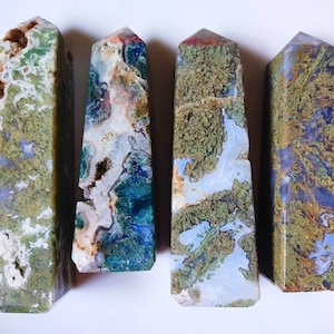May include: Four green, blue, and white agate crystal points with a polished finish. The points are arranged in a row on a white surface.