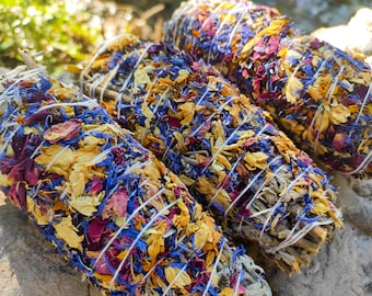 May include: Three bundles of dried herbs and flower petals tied with twine. The bundles are a mix of yellow, blue, and purple flowers.