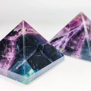 Può includere: Due piramidi di cristallo di fluorite di colore viola, blu e verde. Le piramidi sono realizzate in cristallo naturale e hanno una finitura liscia e lucida.