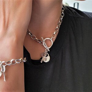May include: A silver chain necklace and bracelet with a padlock and key charm. The necklace and bracelet have a toggle clasp.