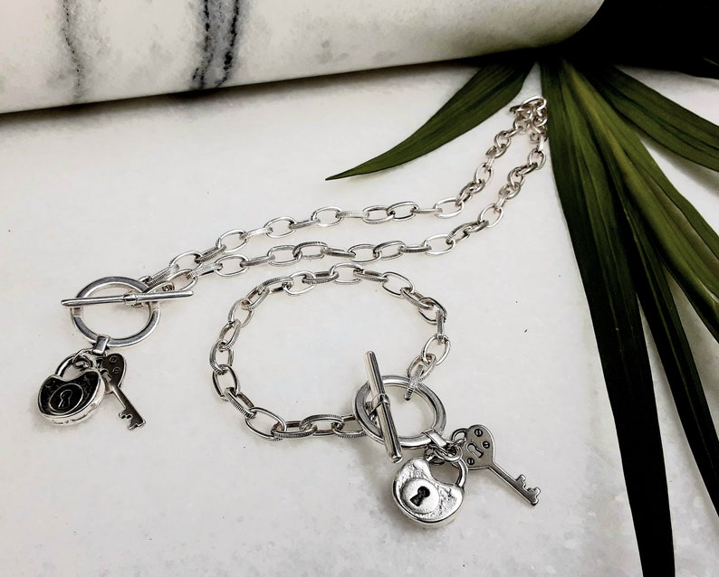 May include: A silver necklace and bracelet set with lock and key charms. The necklace and bracelet feature a toggle clasp.