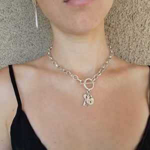 May include: A silver chain necklace with a toggle clasp and a heart-shaped padlock charm with a key attached.