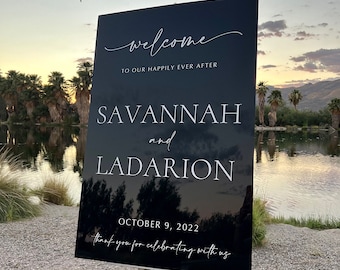 May include: Black welcome sign with white text. The sign reads "Welcome to our happily ever after Savannah and Ladarion October 9, 2022 Thank you for celebrating with us".