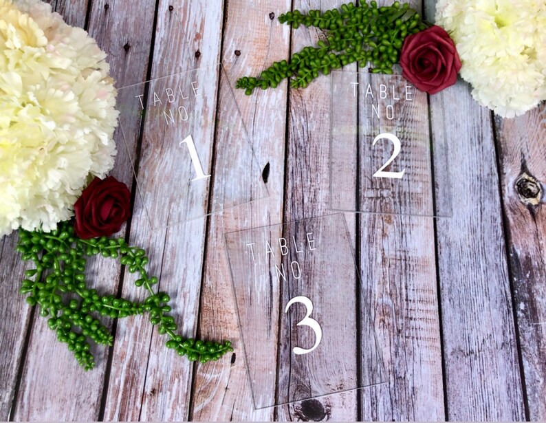 May include: Three clear acrylic table number signs with white text. The signs read "Table No. 1", "Table No. 2", and "Table No. 3".
