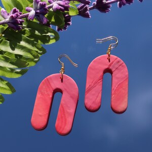 Op de afbeelding: Een paar roze en witte marmeren boogvormige oorbellen met gouden haakjes.