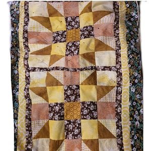 Könnte beinhalten: Eine Steppdecke mit Patchwork-Muster aus braunem, gelbem und weißem Stoff. Die Steppdecke ist mit Stecknadeln befestigt und hat einen floralen Rand.