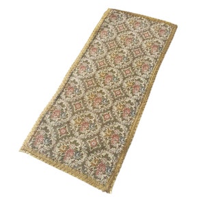 Könnte beinhalten: Ein langer, rechteckiger Tischläufer mit einem floralen Muster in Rosa-, Blau- und Grüntönen. Der Läufer hat einen goldenen Fransenrand.