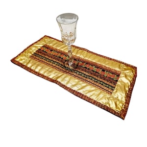 Könnte beinhalten: Ein gold- und brauner Tischläufer mit einem floralen Muster und einem klaren Glas darauf.
