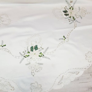 May include: White round tablecloth with a scalloped edge and embroidered Christmas designs. The design features poinsettia flowers, holly leaves, and candles.