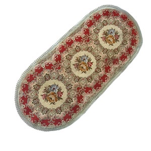Könnte beinhalten: Ovaler Tischläufer mit rotem Hintergrund und beigefarbenem Blumenmuster. Der Läufer hat einen silbernen Fransenrand.