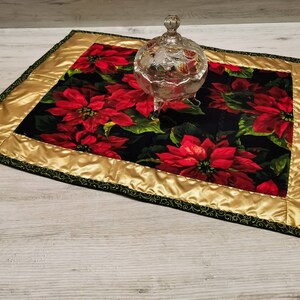 Könnte beinhalten: Ein goldfarbener und grüner gesteppter Tischläufer mit schwarzem Hintergrund und einem roten Weihnachtsstern-Muster. Der Läufer ist mit einem goldfarbenen Satinbesatz und einem grünen gewellten Rand verziert.