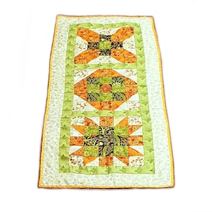 Könnte beinhalten: Ein grüner, orangefarbener und weißer Patchwork-Tischläufer mit Blumenmuster. Der Läufer hat drei quadratische Paneele mit unterschiedlichen Designs.