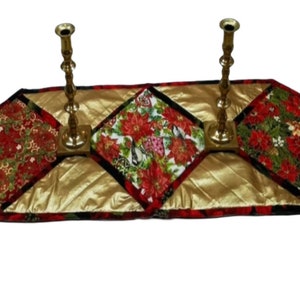 Könnte beinhalten: Ein gesteppter Tischläufer mit goldfarbenem Hintergrund und vier quadratischen Mustern in Rot und Grün. Zwei goldene Kerzenhalter sind auf dem Läufer platziert.