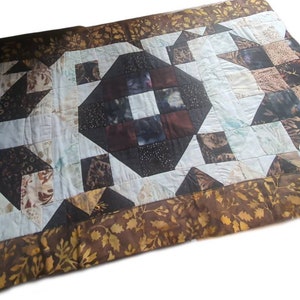 Könnte beinhalten: Eine handgefertigte Steppdecke mit einem zentralen Rautenmuster in Braun-, Schwarz- und Weißtönen. Die Steppdecke hat einen Rand mit einem Blattdesign. Das Patchwork-Design umfasst verschiedene geometrische Formen und Muster.