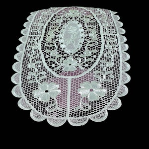 May include: White oval lace table runner with a floral design. The lace is delicate and intricate, with a scalloped edge.