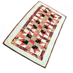 Könnte beinhalten: Eine weiße Steppdecke mit einem roten, schwarzen und goldenen Sternenmuster. Die Steppdecke ist aus Stoffresten gefertigt und hat einen weißen Rand.