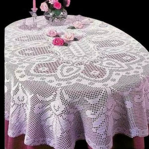 Könnte beinhalten: Weiße Häkeltischdecke mit Blumenmuster. Die Tischdecke ist rund und hat einen gewellten Rand. Sie liegt auf einem Tisch mit einer rosa Tischdecke darunter.