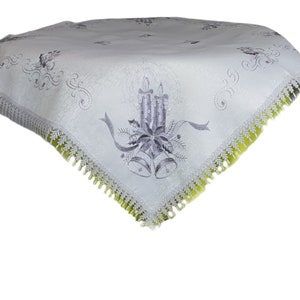May include: White tablecloth with a silver embroidered design of candles, bells, and holly. The tablecloth has a green lace trim.