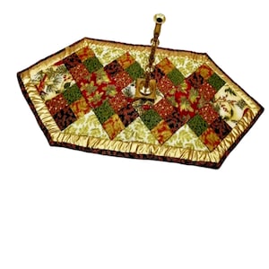 Könnte beinhalten: Ein sechseckiger Tischläufer mit Patchwork-Design aus roten, grünen, goldenen und schwarzen Stoffen. Der Läufer hat einen goldenen Satinbesatz und ist mit einem goldenen Kerzenständer verziert.