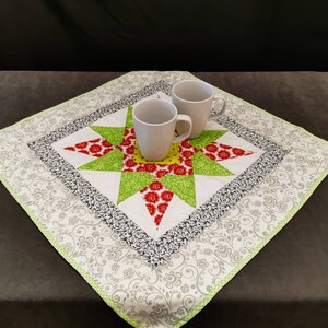 Könnte beinhalten: Ein weißer Tischläufer mit einem grün-rot-gelben Sternmuster. Zwei weiße Keramikbecher stehen auf dem Läufer.