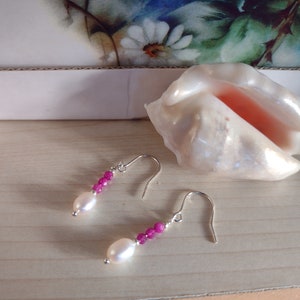 Könnte beinhalten: Ein Paar silberne Ohrringe mit rosa Perlen und einer weißen Perle an jedem Ohrring.