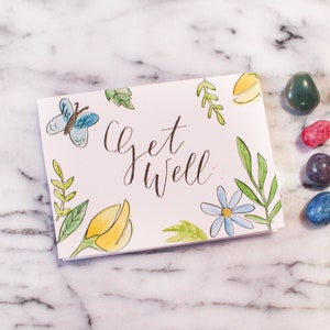 Cartão de flores de borboleta com letras à mão em aquarela, cartão de melhoras, cartão de simpatia, cartão de felicitações de melhoras em breve