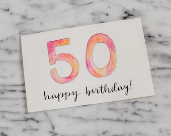 May include: A watercolor card with the number 50 in pink and orange, with the words "happy birthday!" written in black ink.