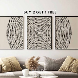 May include: Three black framed prints with a beige background and a black and white geometric pattern. The prints are hanging on a white wall above a gray couch with pillows and two gold metal side tables.