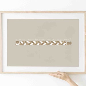 Op de afbeelding: Een ingelijst print met een beige achtergrond en een wit en bruin gevlochten ontwerp in het midden. De tekst "Alles gebeurt met een reden" staat in wit cursief boven de vlecht.