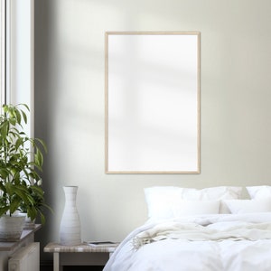 May include: A white bed with a white blanket and pillows, a wooden frame picture hanging on the wall above the bed, and a vase on a wooden table next to the bed.