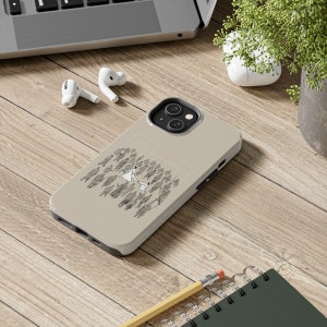 May include: A beige phone case with a black outline and a white illustration of a couple dancing in a crowd of people. The phone case has a camera cutout and a raised camera bump.