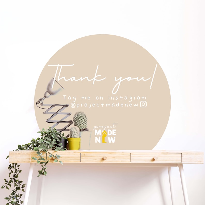 Puede incluir: Un c&iacute;rculo beige con el texto "Thank you!" y "Tag me on instagram @projectmadenew" en una pared blanca. Hay dos peque&ntilde;as plantas de cactus en macetas y una l&aacute;mpara sobre un escritorio de madera en primer plano.