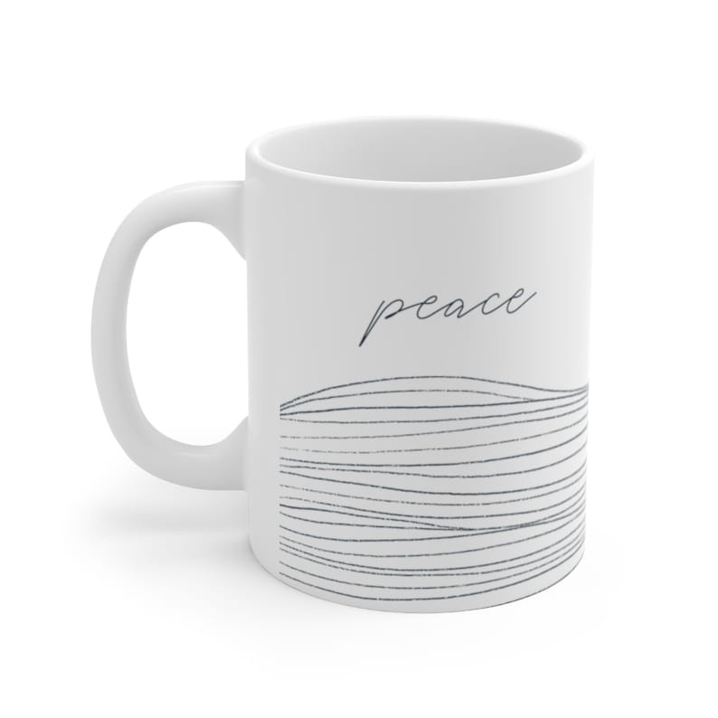 May include: White ceramic mug with a black and white abstract design and the word "peace" in cursive.