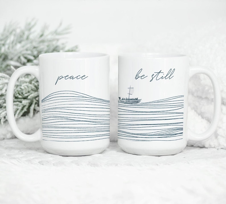 May include: Two white ceramic mugs with black text and a wavy line design. The mug on the left says "peace" and the mug on the right says "be still".